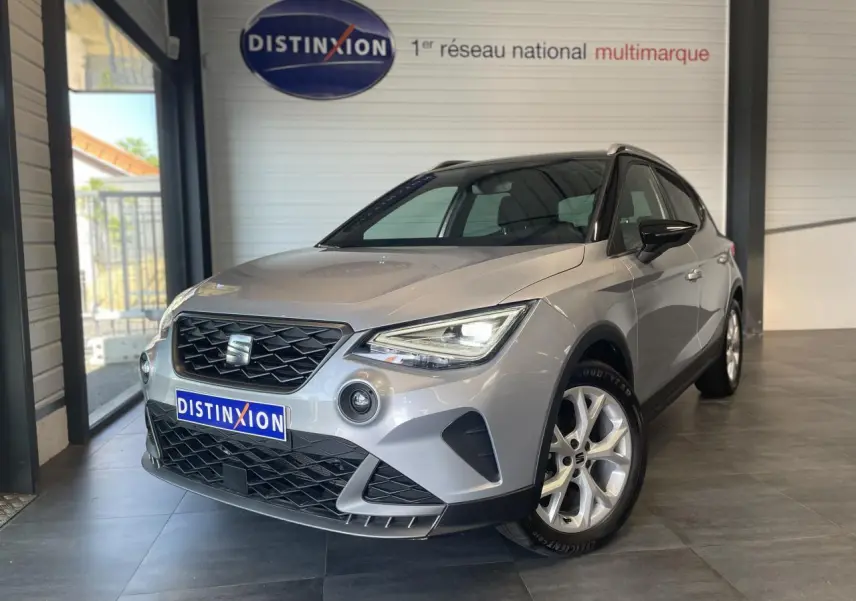 SEAT Arona 2024 gris GRS en 3/4 avant droit, avec calandre noire et jantes alliage 16 pouces visibles en showroom.