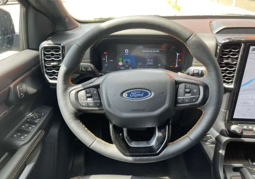 Vue intérieure centrée sur le volant du Ford Ranger 2025 noir agate, avec tableau de bord numérique et écran tactile visible.