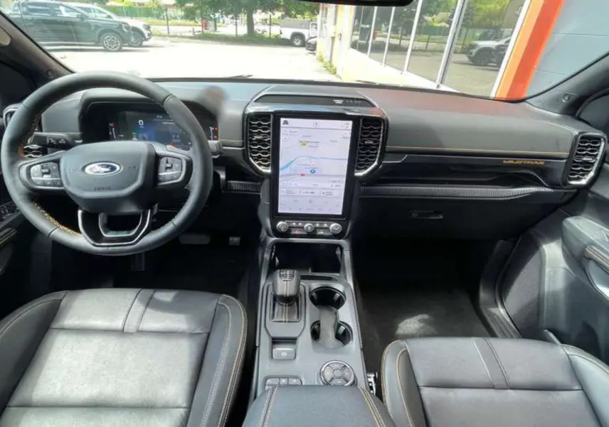 Vue intérieure du Ford Ranger 2025 Wildtrak Plus, tableau de bord noir avec écran tactile vertical et sellerie cuir noire.