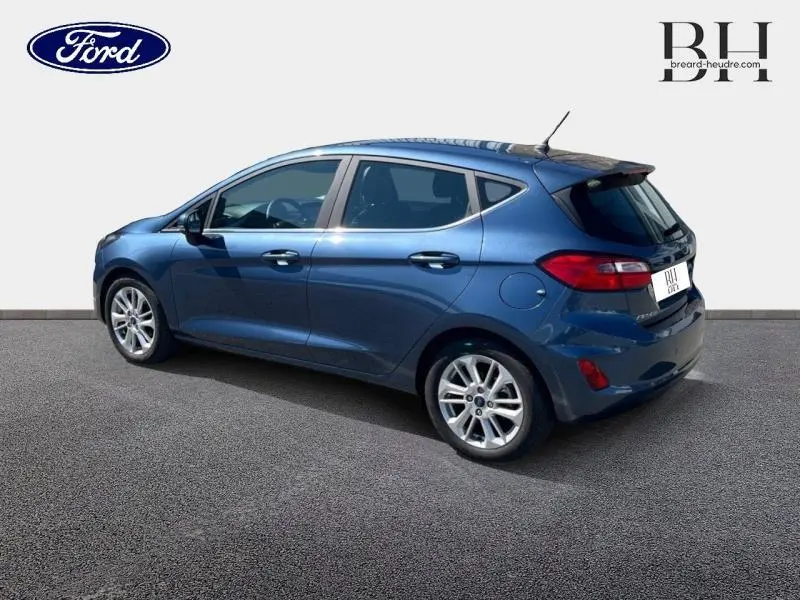 Vue 3/4 arrière droite d'une Ford Fiesta 2022 bleu azur métallisé avec jantes alliage et becquet arrière.