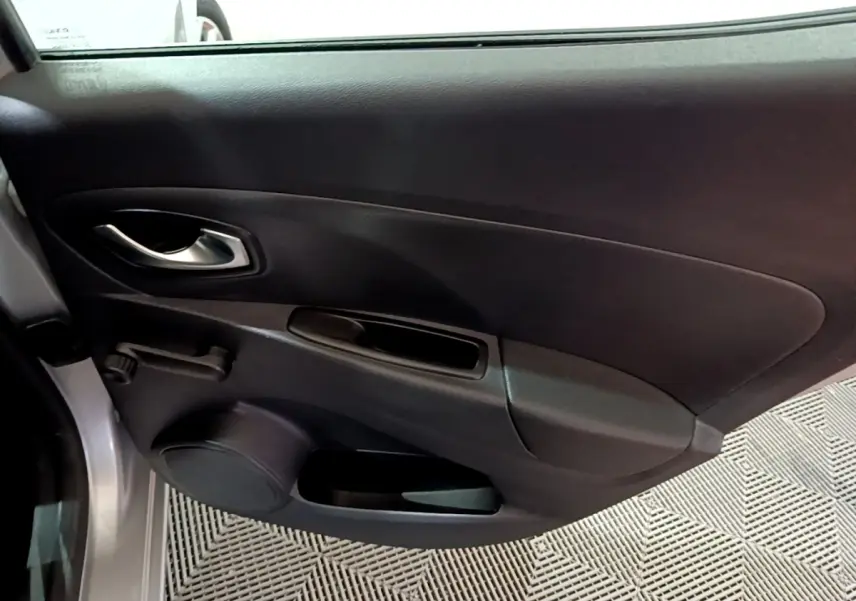 Vue intérieure côté gauche de la porte avant d’une Renault Clio gris clair, avec poignée argentée et commande manuelle de vitre.