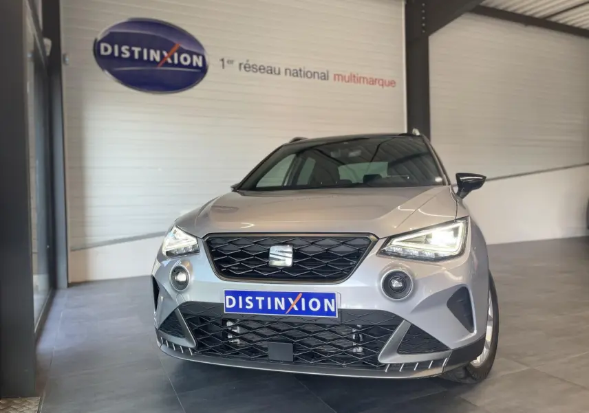 Vue de face d'une SEAT Arona 2024 gris GRS avec calandre noire et phares allumés en showroom.