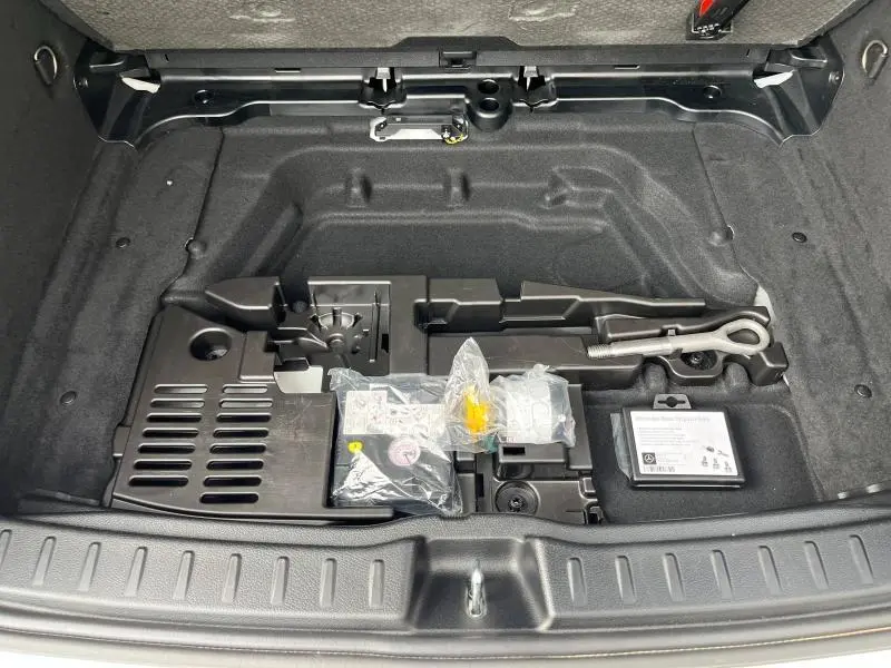Vue plongeante sur le coffre ouvert du Mercedes GLA 200 AMG Line 2022, montrant le rangement sous plancher avec outils et kit de réparation.