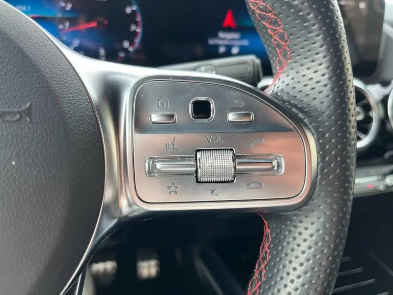 Gros plan sur les commandes du volant cuir noir perforé avec surpiqûres rouges du Mercedes GLA 200 AMG Line blanc polaire.