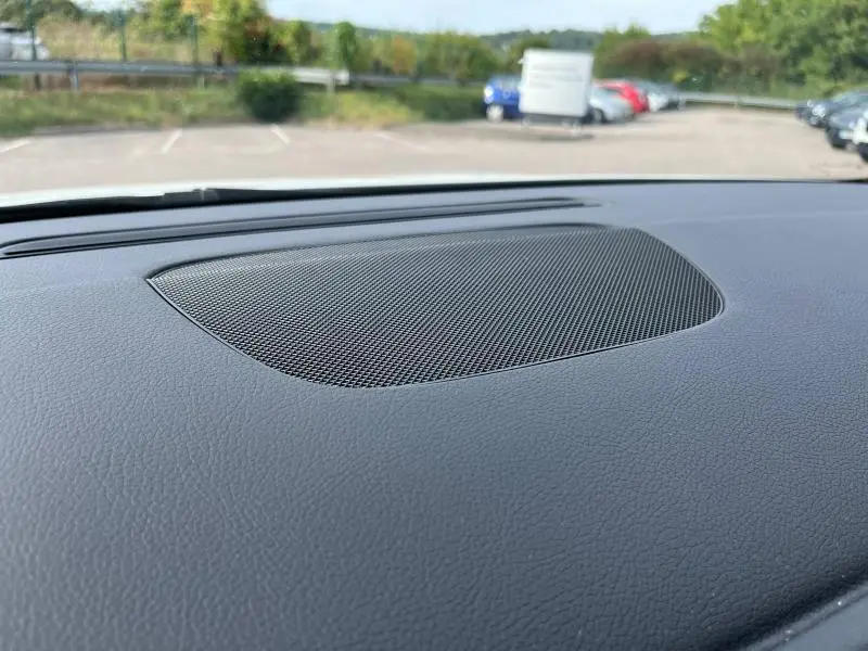 Gros plan sur la grille de haut-parleur intégrée au tableau de bord noir du Mercedes GLA blanc polaire, vue vers l'avant.