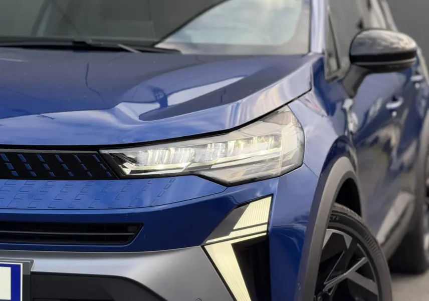 Gros plan sur l'avant droit du Renault Captur Bleu Iron, mettant en valeur le phare LED et la calandre moderne.