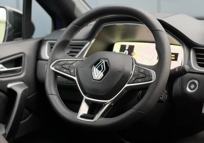 Gros plan sur le volant noir avec surpiqûres tricolores du Renault Captur Bleu Iron, tableau de bord numérique en arrière-plan.