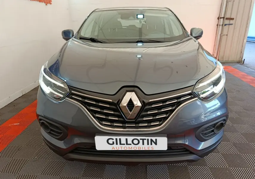 Vue avant rapprochée d’un Renault Kadjar gris foncé avec phares allumés et calandre chromée visible.