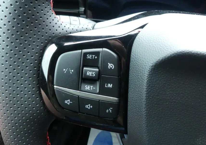 Gros plan sur les commandes noires du volant perforé avec surpiqûres rouges du Ford Puma gris métallisé 2025.