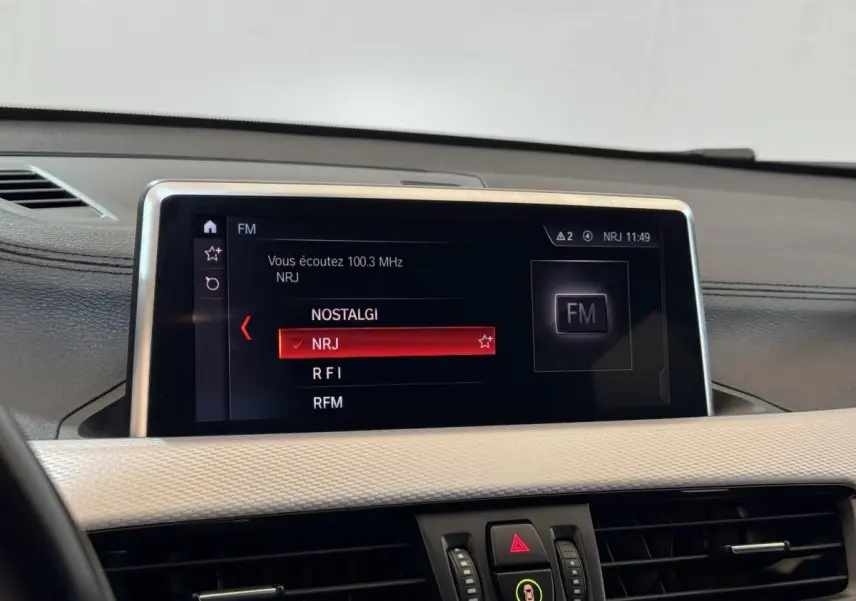 Écran central tactile du tableau de bord de la BMW X2 xDrive25e M Sport, affichant les stations radio FM.