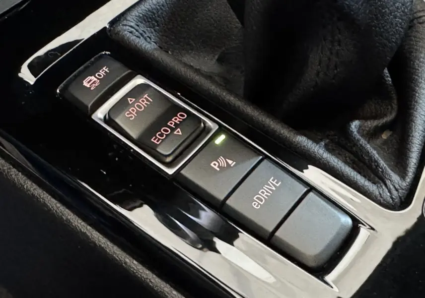 Gros plan sur les boutons de mode de conduite et assistance au stationnement du BMW X2 xDrive25e bleu 2021.