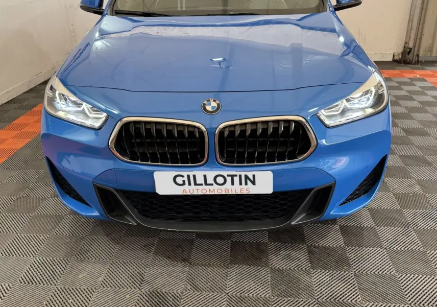Vue frontale rapprochée d'une BMW X2 xDrive25e M Sport bleu avec calandre noire et phares allumés.