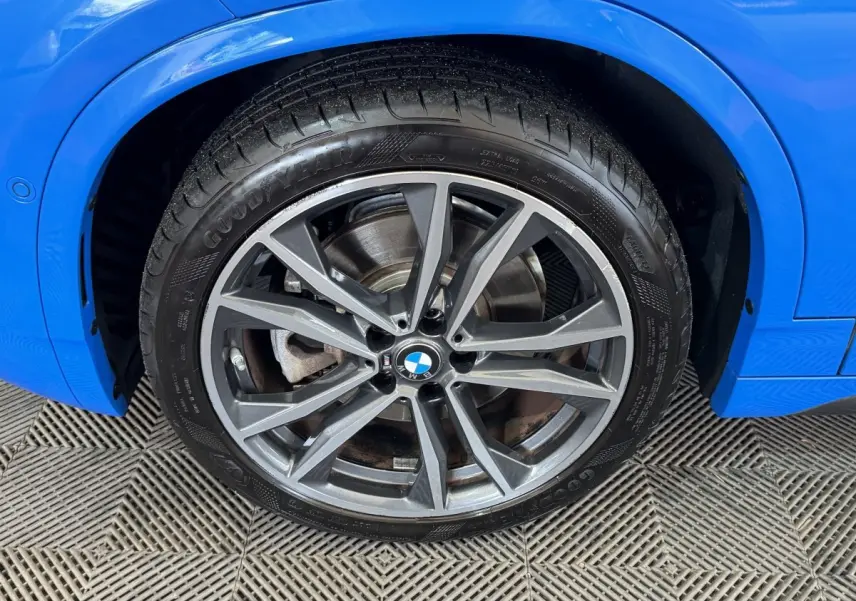 Gros plan sur la roue avant droite d'une BMW X2 bleu électrique avec jante alliage et pneu Goodyear.