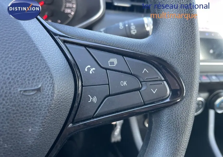 Gros plan sur les commandes au volant côté gauche d'une Renault Clio Société blanc glacier, tableau de bord en arrière-plan.