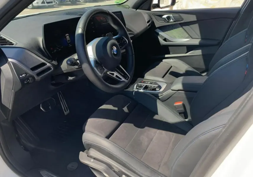 Intérieur côté conducteur de la BMW Série 1 118d 2025, sellerie Alcantara noire avec surpiqûres bleues et volant M cuir.