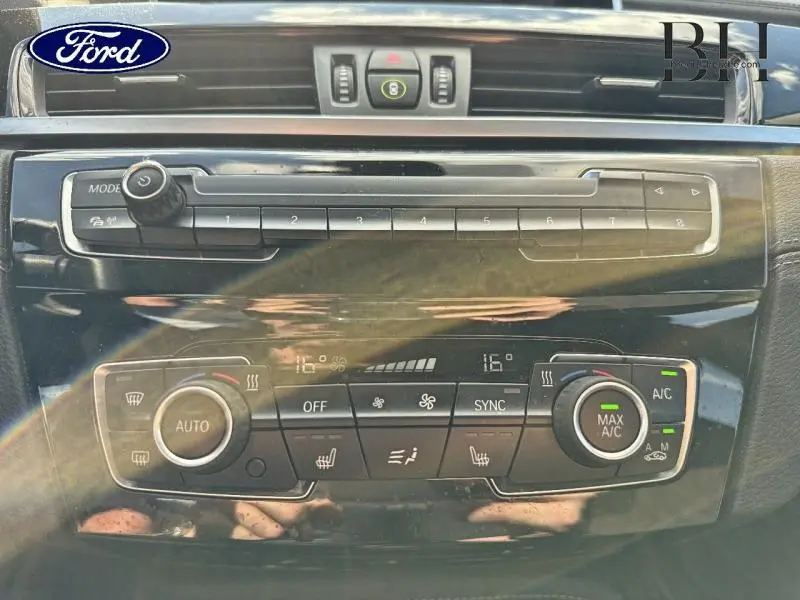 Tableau de bord noir brillant du BMW X1 xDrive25e 2021 avec commandes climatisation et audio en gros plan.