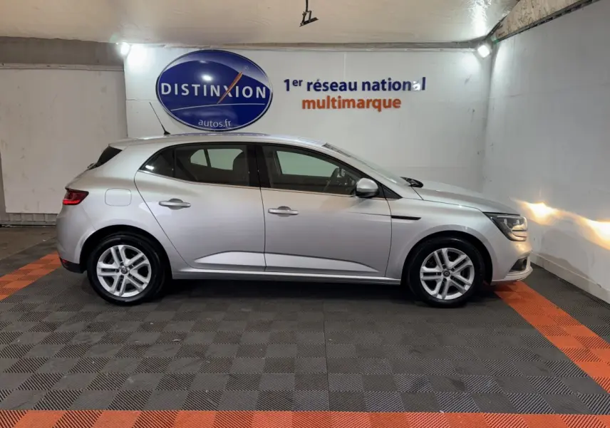 Profil droit d'une Renault Mégane Business gris clair, stationnée en intérieur sur sol noir et orange.