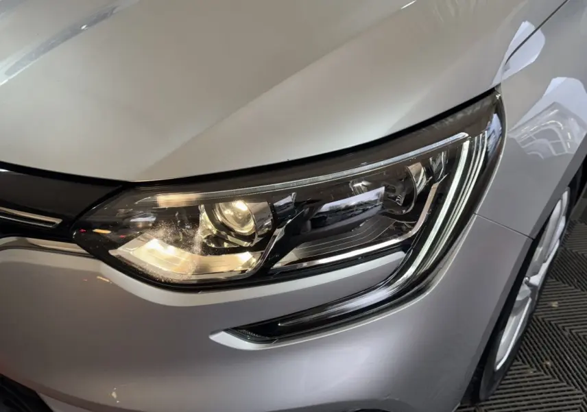 Gros plan sur le phare avant droit d’une Renault Mégane Business gris clair, mettant en valeur les LED et la carrosserie lisse.