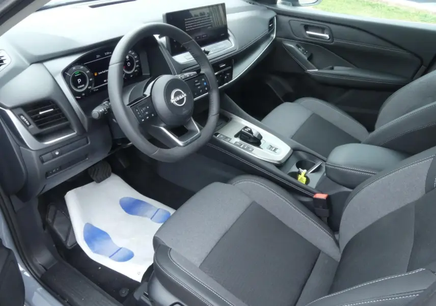 Vue intérieure côté conducteur du Nissan Qashqai 1.5 e-Power 2025 avec sellerie gris foncé et tableau de bord numérique.