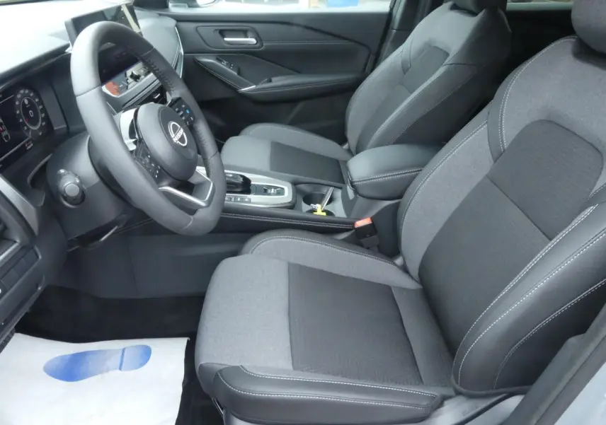 Vue intérieure côté conducteur du Nissan Qashqai 1.5 e-Power 2025 avec sièges gris bi-matière et console centrale.