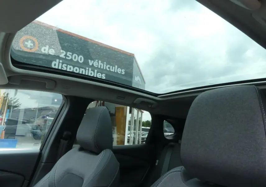 Vue intérieure du Nissan Qashqai 2025 gris, mettant en valeur le toit panoramique en verre et les sièges avant en tissu gris.