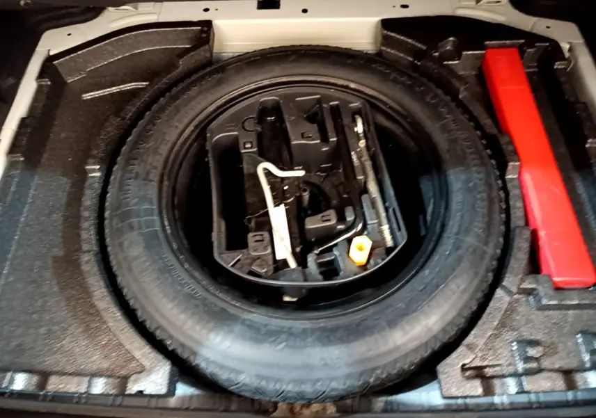 Vue rapprochée de la roue de secours et des outils dans le coffre d'une Peugeot 308 blanche de 2017.