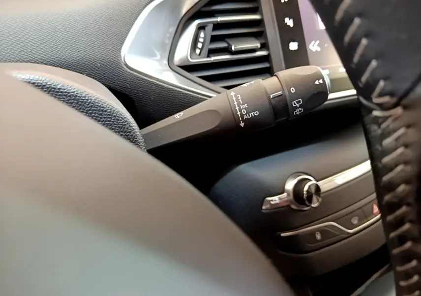 Gros plan sur la manette d'essuie-glace côté gauche du tableau de bord noir d'une Peugeot 308 blanche de 2017.