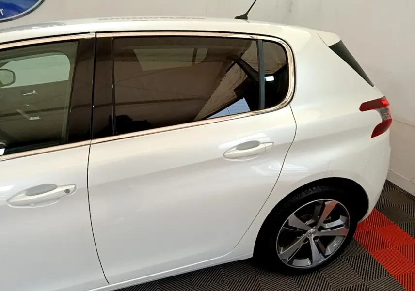 Vue latérale côté droit d'une Peugeot 308 blanche, mettant en valeur les vitres teintées et les jantes alliage.
