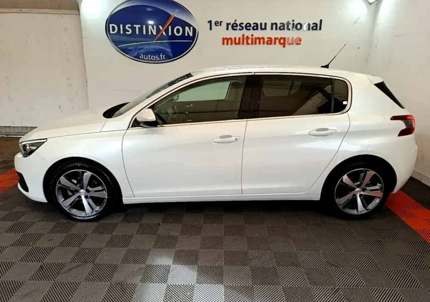 Profil côté gauche d'une Peugeot 308 blanche 2017, avec jantes alliage et vitres teintées, en intérieur showroom.