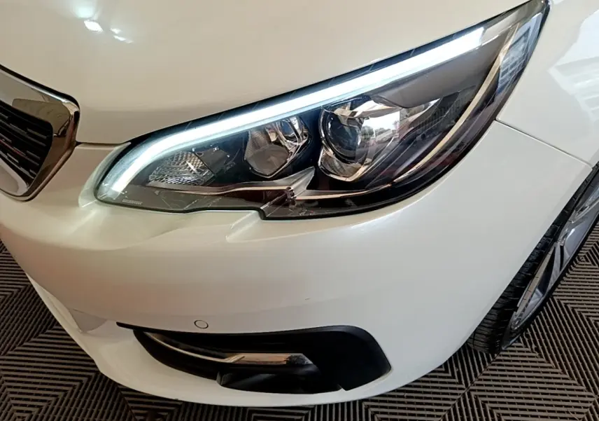 Gros plan sur le phare avant droit blanc d'une Peugeot 308 2017 avec feux LED et calandre partielle visible.