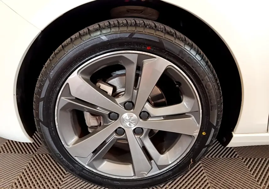 Gros plan sur la roue avant droite d'une Peugeot 308 blanche, mettant en valeur la jante alliage grise et le logo lion central.