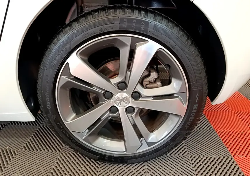 Gros plan sur la roue avant droite d'une Peugeot 308 blanche, avec jante alliage et logo lion au centre.
