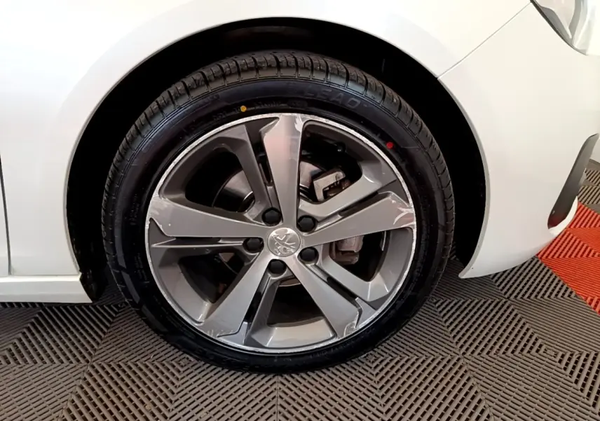 Gros plan sur la roue avant droite d'une Peugeot 308 blanche, mettant en valeur la jante alliage gris et le pneu neuf.