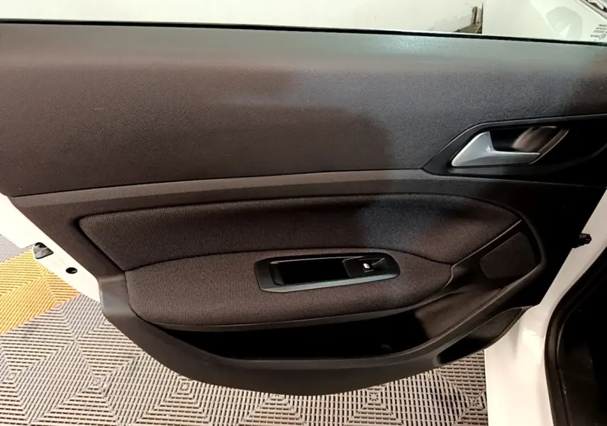Vue intérieure de la porte côté gauche d'une Peugeot 308 blanche, avec habillage tissu noir et commande de vitre électrique.