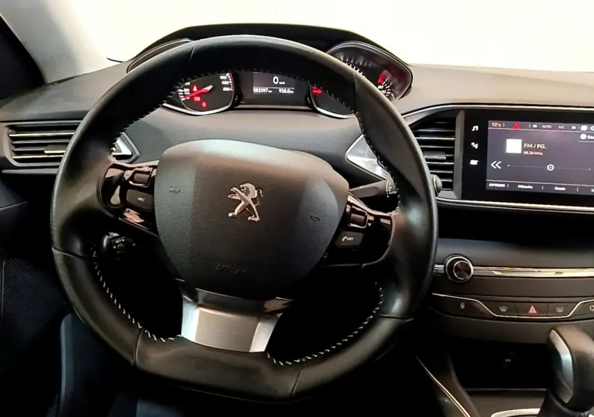 Vue intérieure centrée sur le volant cuir et le tableau de bord avec écran tactile de la Peugeot 308 blanche de 2017.