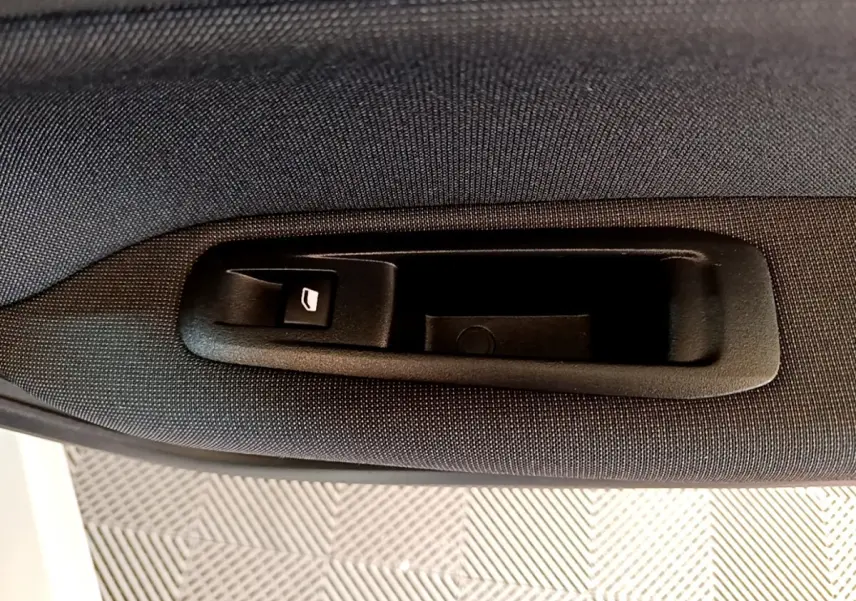 Poignée intérieure de coffre noir sur tissu gris foncé dans une Peugeot 308 blanche, vue en gros plan.