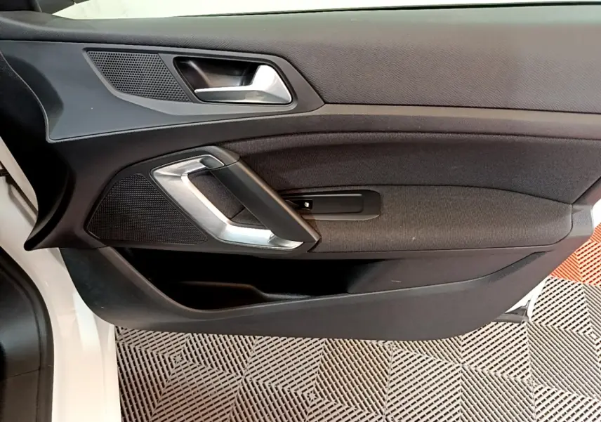 Vue rapprochée de la porte intérieure côté conducteur d’une Peugeot 308 blanche, avec poignée argentée et garniture noire.
