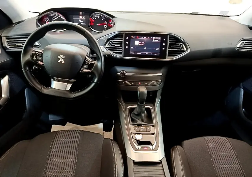 Vue intérieure avant de la Peugeot 308 2017, tableau de bord noir avec écran tactile central et volant cuir multifonctions.