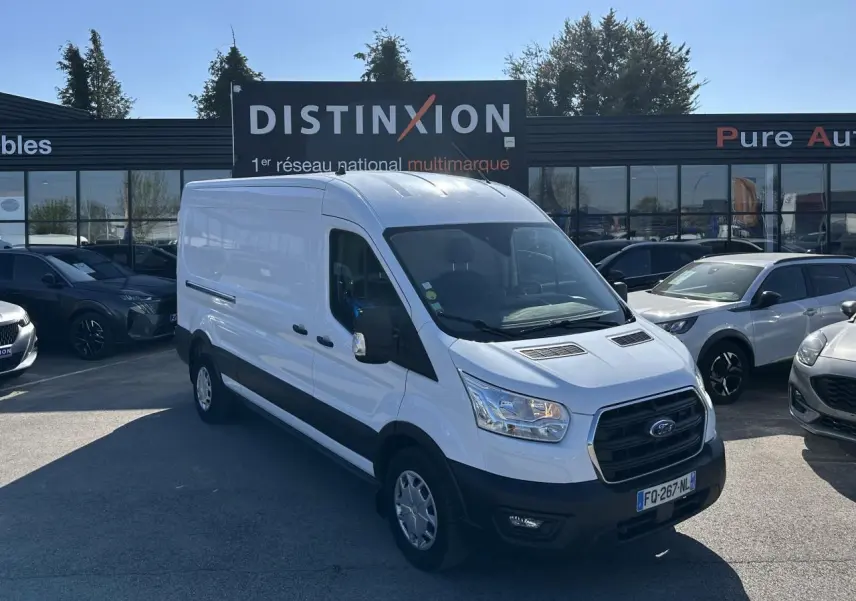 Ford Transit Fourgon blanc vu en 3/4 avant droit sur un parking devant un bâtiment commercial.