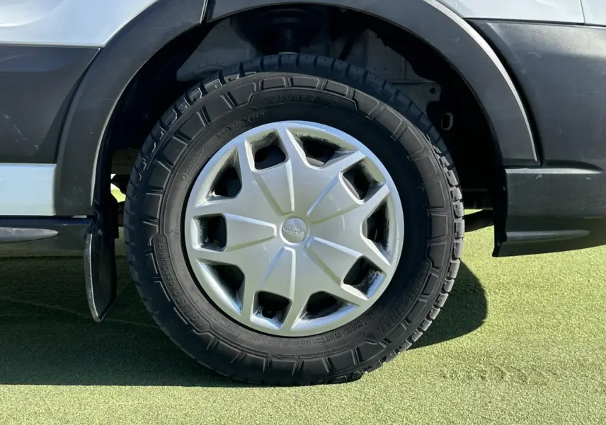 Gros plan sur la roue arrière gauche du Ford Transit Fourgon blanc, avec enjoliveur argenté et pneu tout-terrain.