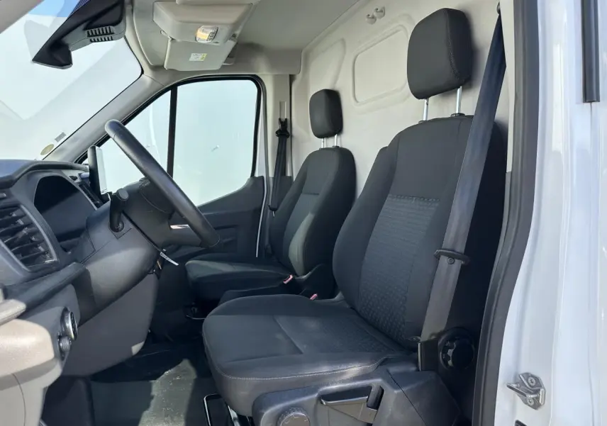 Vue intérieure côté conducteur du Ford Transit Fourgon blanc 2020, montrant les sièges noirs et le volant.