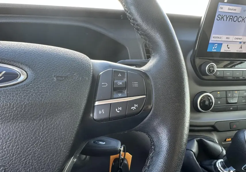 Gros plan sur le volant noir et la console centrale du Ford Transit Fourgon blanc, avec écran tactile affichant Skyrock.