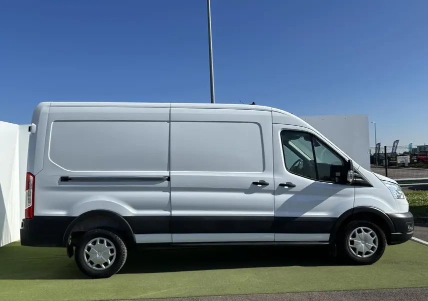 Ford Transit Fourgon blanc vu de profil côté gauche, avec bandes noires sur les bas de caisse et enjoliveurs pleins.