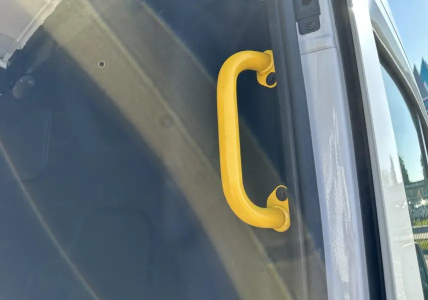 Poignée de maintien jaune visible sur l'ouverture latérale droite du fourgon blanc Ford Transit 2020.