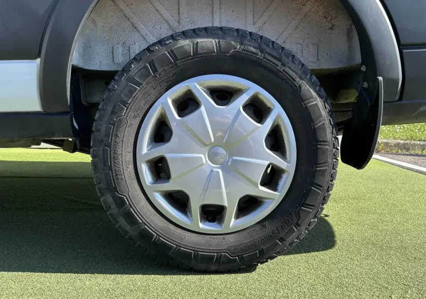 Gros plan sur la roue arrière droite du Ford Transit Fourgon blanc, avec enjoliveur argenté et pneu tout-terrain.