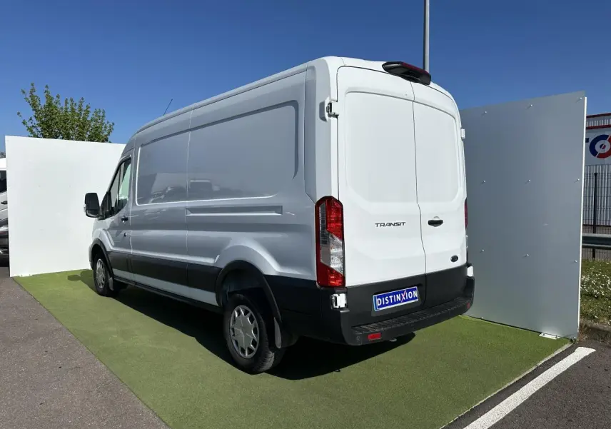 Fourgon Ford Transit blanc en vue 3/4 arrière droit, avec pare-chocs noir et porte latérale coulissante visible.