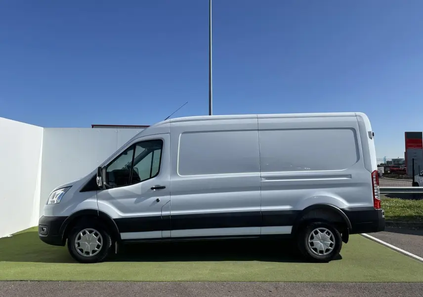 Profil côté gauche d'un fourgon Ford Transit blanc avec jantes acier et bande noire sur bas de caisse.