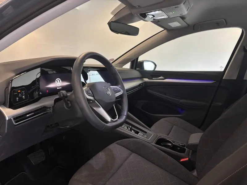 Intérieur avant droit de la Volkswagen Golf 2024 avec sièges tissu Maze noir et éclairage d'ambiance bleu sur la portière