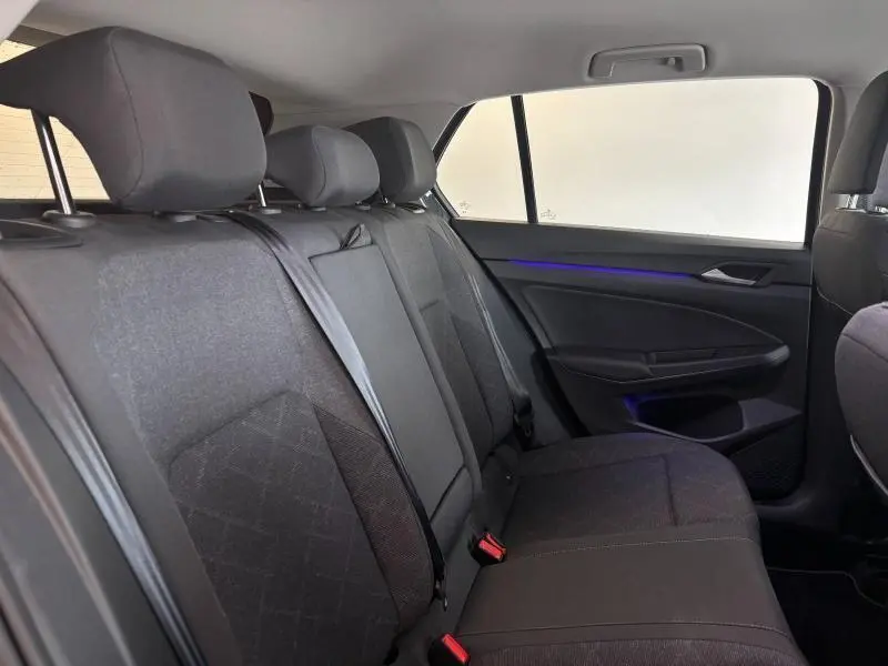Vue intérieure côté droit de la banquette arrière en tissu noir avec éclairage d'ambiance bleu d'une Volkswagen Golf 2024 gris dauphin métallisé.