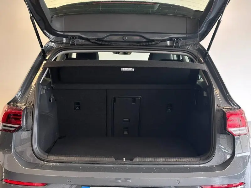 Coffre ouvert vu de l'arrière d'une Volkswagen Golf 2024 gris dauphin métallisé avec banquette arrière et cache-bagages.